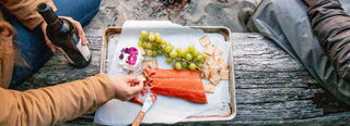 A picnic at the beach set on a metal tray with smoked salmon, grapes, cheese, and crackers