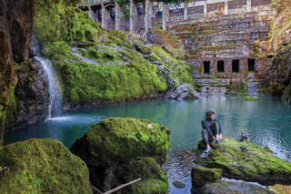 Diver sitting on a large moss-covered rock at edge of dam