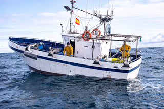 Two fishermen on their boat wearing orange slickers and one is hosing down fish