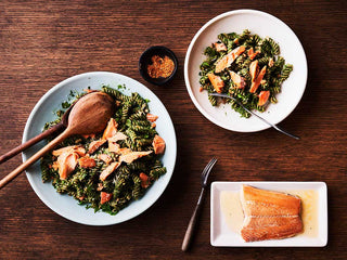 Two white ceramic bowls filled with spinach pesto and fusilli pasta and wild sockeye salmon