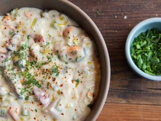 A bowl of white chowder with chunky bits of potato, celery, and mussels