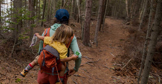 A person hikes through trees carrying a child in a pack