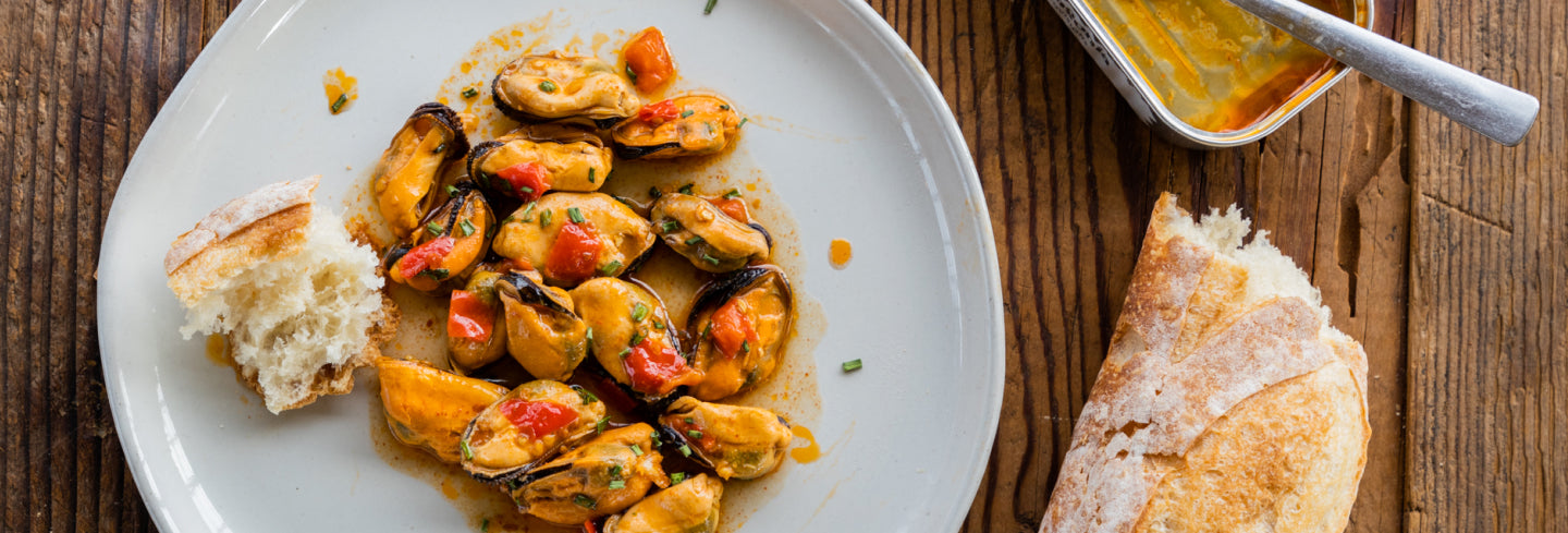 Spicy mussels on a white plate with some bread.