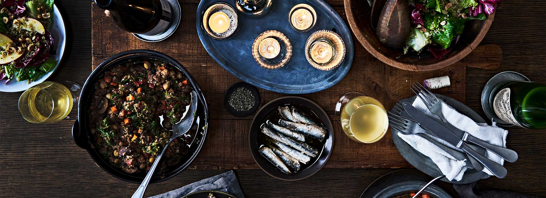 A holiday table is covered with lit candles and dishes of grains, salads, vegetables, and fish, made with Patagonia Provisions foods