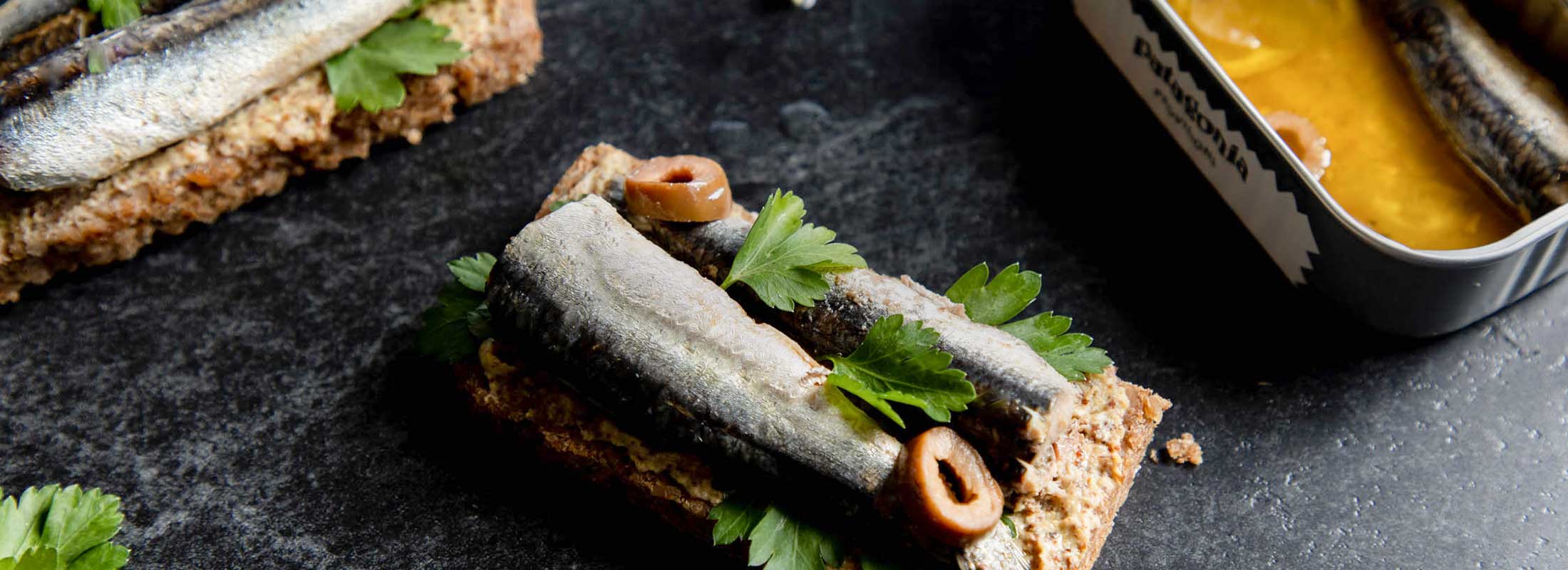 Open faced toasts topped with Patagonia Provisions anchovies, herbs, and olives