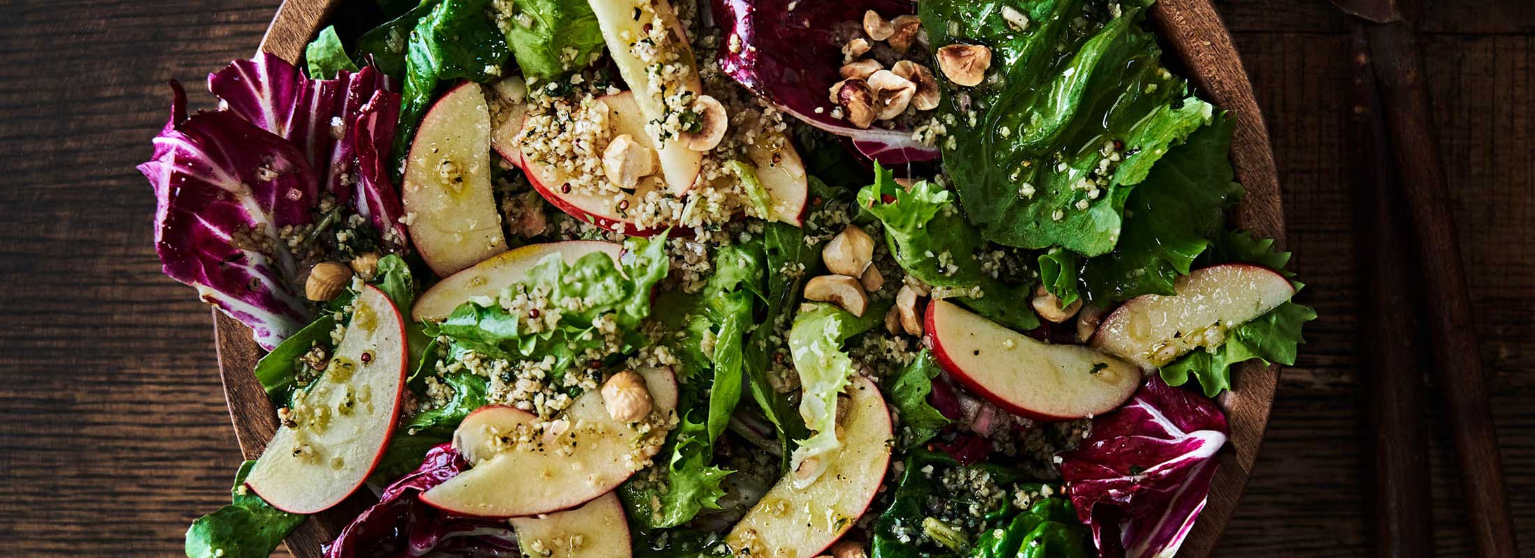 Close shot of a mixed green salad topped with apple slices and Patagonia Provisions Savory Grains