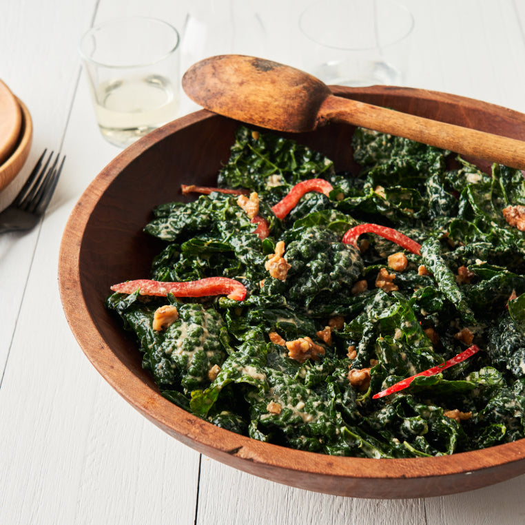 A large wooden serving bowl is overflowing with mixed greens, sliced apples and topped with nuts and Patagonia Provisions savory grains