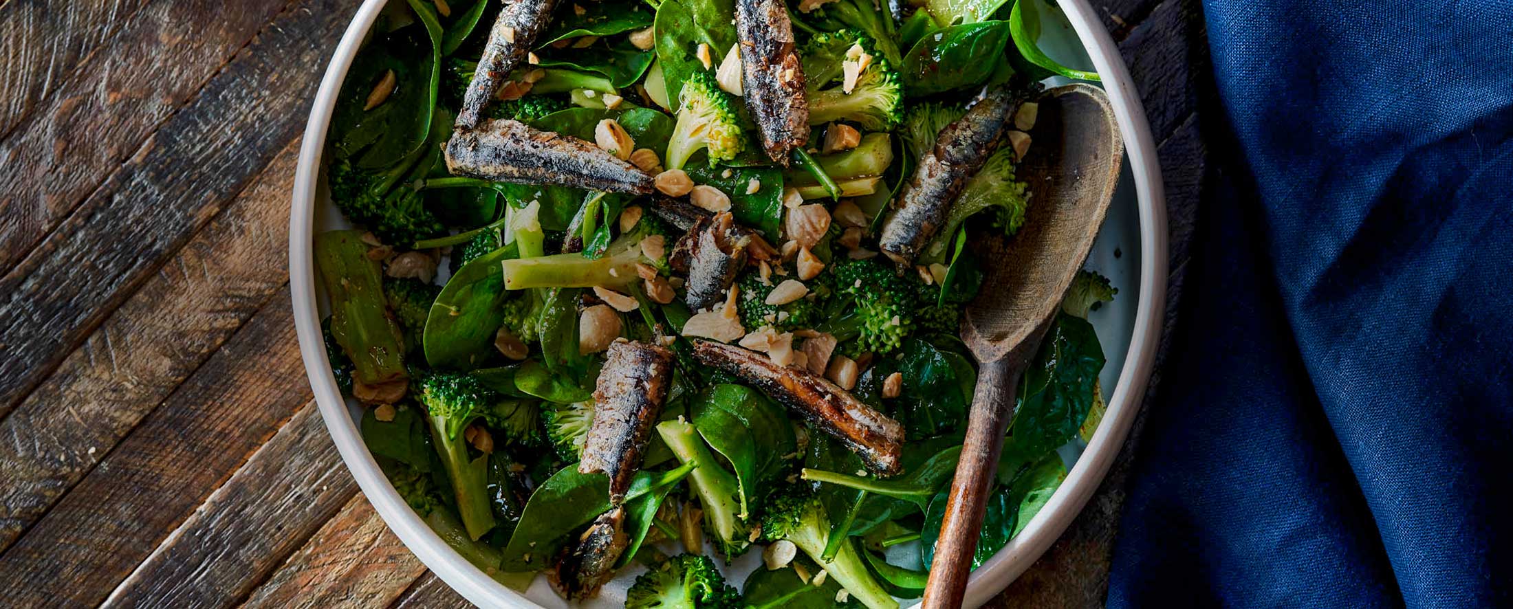 A bowl of dark green salad topped with Patagonia Provisions tinned anchovies, nuts, and broccoli