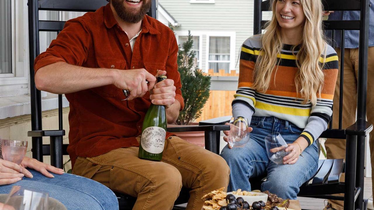 Friends gather on the porch to open a bottle of Patagonia Provisions Cider and enjoy fresh fruits and savory snacks