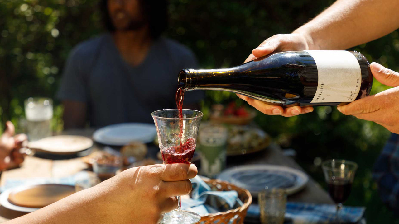 Pouring red wine from Patagonia Provisions into an outstretched glass at a dinner set outside