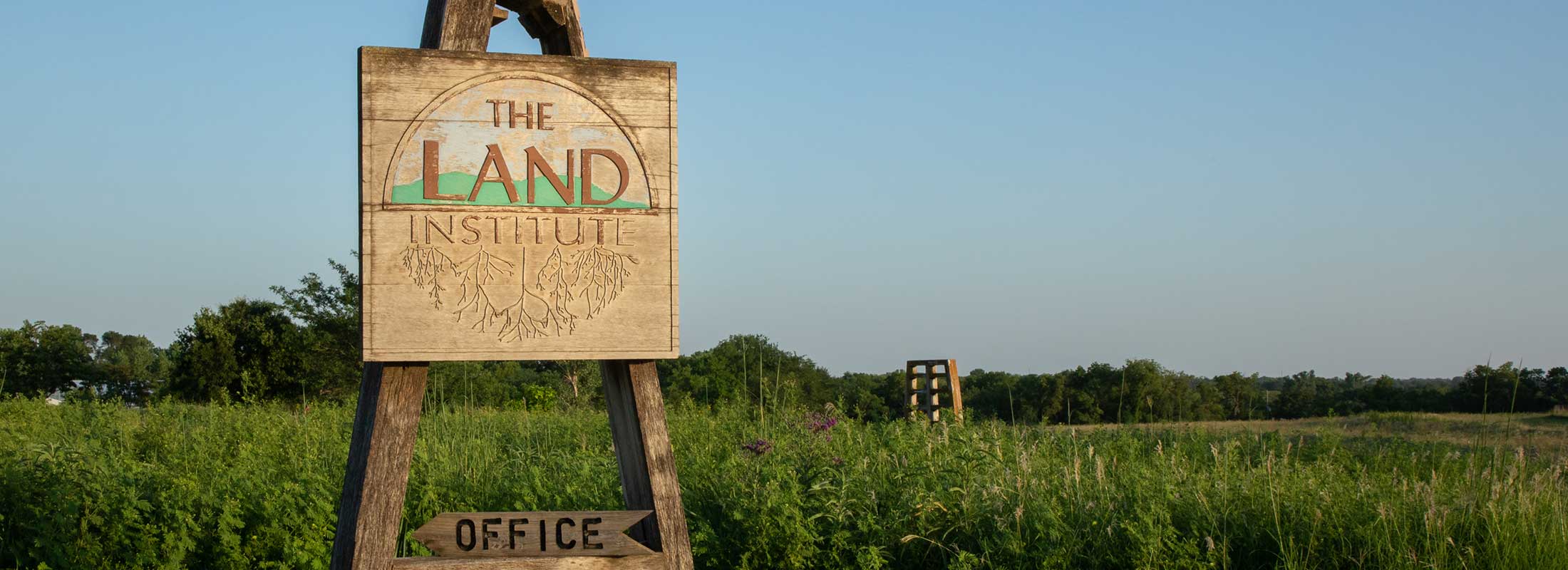 A wooden sign for The Land Institute stands in front of a field of wild perennial grasses and flowers
