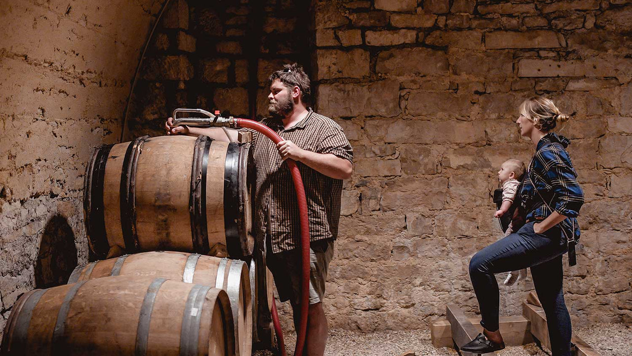 Vintners tap a barrel in a stone walled room