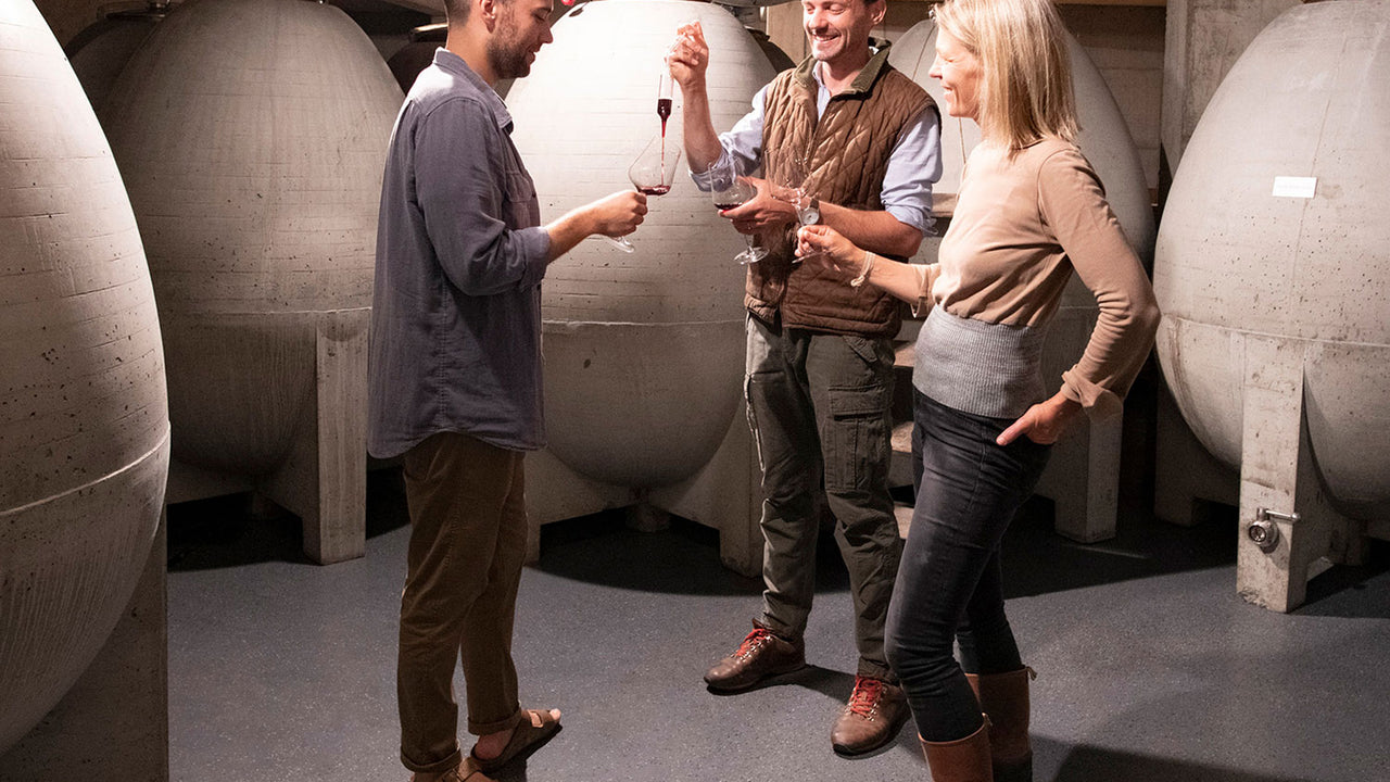 Three people sampling wine in a cellar, surrounded by egg-shaped tanks