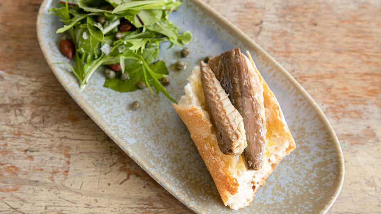 An oblong ceramic dish with salad and piece of baguette topped with Patagonia Provisions Smoked Atlantic Salmon