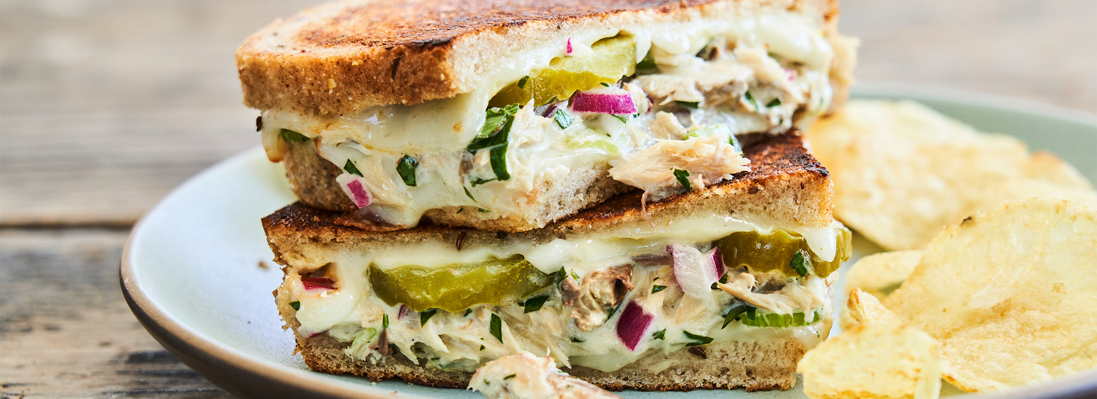 Stacked halves of a mackerel melt sandwich on a ceramic plate beside potato chips