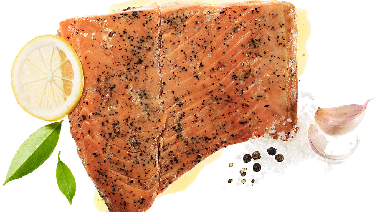 A fillet of Patagonia Provisions Wild Pink Salmon with lemon slice, garlic cloves, and peppercorns, on a white background