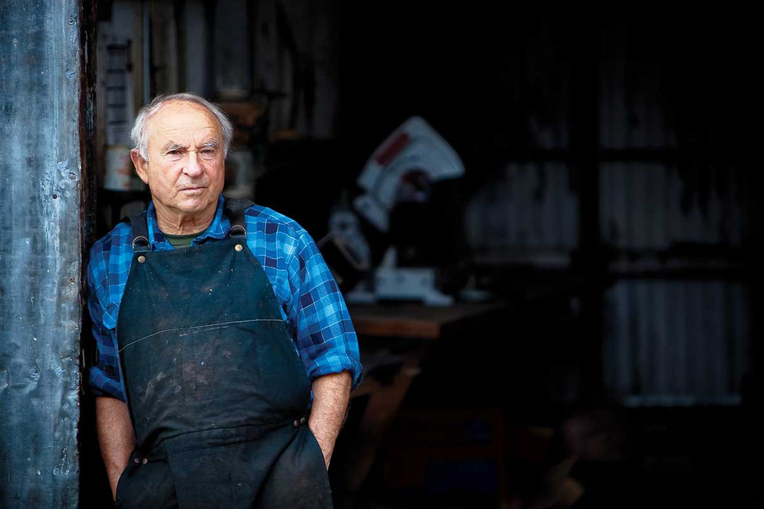Yvon Chuinard stands at the doorway to a work shed, wearing a blue checked shirt and heavy work apron