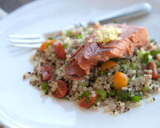 A plate of quinoa with cherry tomatoes, green onions, and a pice of salmon on top