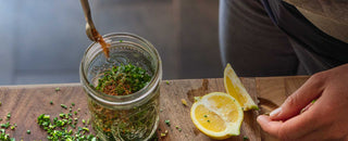 Person sprinkles Patagonia Provisions Aji Molido spice into a jar with fresh herbs and lemon to make homemade chimichurri sauce