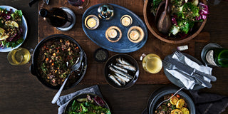 A holiday table, lit by candles, is covered with dishes of food and bottles of wine