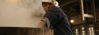 A brewmaster at Terada Honke reaches into a wooden vat of steaming rice