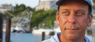 Author Paul Greenberg, wearing a baseball cap in front of a seaside background