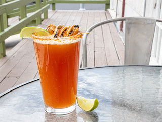 A tall dark orange Aji Molido Michelada cocktail in a pint glass topped with a skewer of Patagonia Provisions Savory Sofrito Mussels