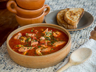 A tomato-rich stew with chunks of salmon in a wooden bowl with pieces of toasted bread on the side