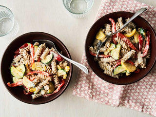 Two bowls of fusilli pasta with vegetables and blue cheese sauce on a patterned cloth