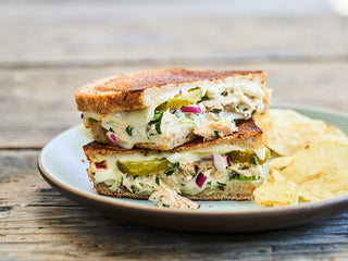 Grilled Canned Mackerel salad sandwich with melted cheese, potato chips on a white plate