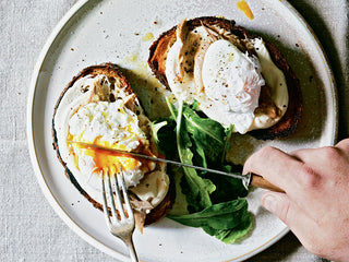 Hands cutting into slices of toast topped with poached egg and Patagonia Provisions Mackerel