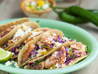 5 small salmon tacos on a green plate topped with goat cheese