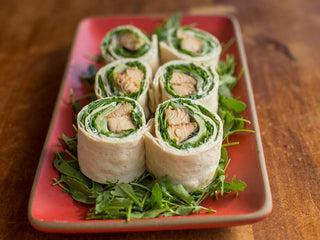 Lavash wrap cut in 6 pinwheels on a rectangular ceramic plate with layers of greens, cucumber, and salmon