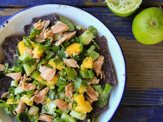 Tortilla chips topped with chunks of mango, cucumber, greens, and salmon in a bowl