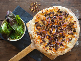 A baked pizza on a board with chanterelle mushrooms, salmon, and purple onion with a side salad