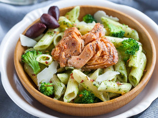 A bowl of seasoned penne pasta with broccoli florets topped with salmon