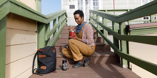 A woman sits on outdoor staircase with green wooden railings, enjoying a meal from Patagonia Provisions insulated canisters