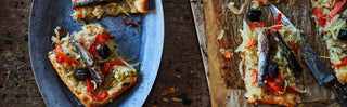 Puff pastry pizzas topped with Patagonia Provisions Spanish White Anchovies, on a blue serving dish and wooden board