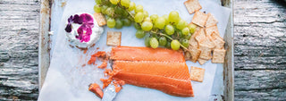 A large fillet of Patagonia Provisions Wild Sockeye Salmon is served outside with cheese, grapes, and crackers on a metal tray with parchment paper