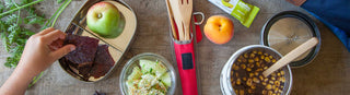 A table set for lunch with Patagonia Provisions organic foods and snacks in canisters beside a bamboo cutlery set and fresh fruit