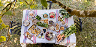 A table and chairs, set outside under a tree, covered with colorful tablecloth and dishes of fresh food