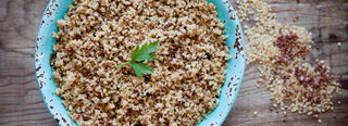 A rustic blue ceramic bowl filled with cooked Patagonia Provisions Mushroom Savory Grains sits on a wooden table beside raw grains