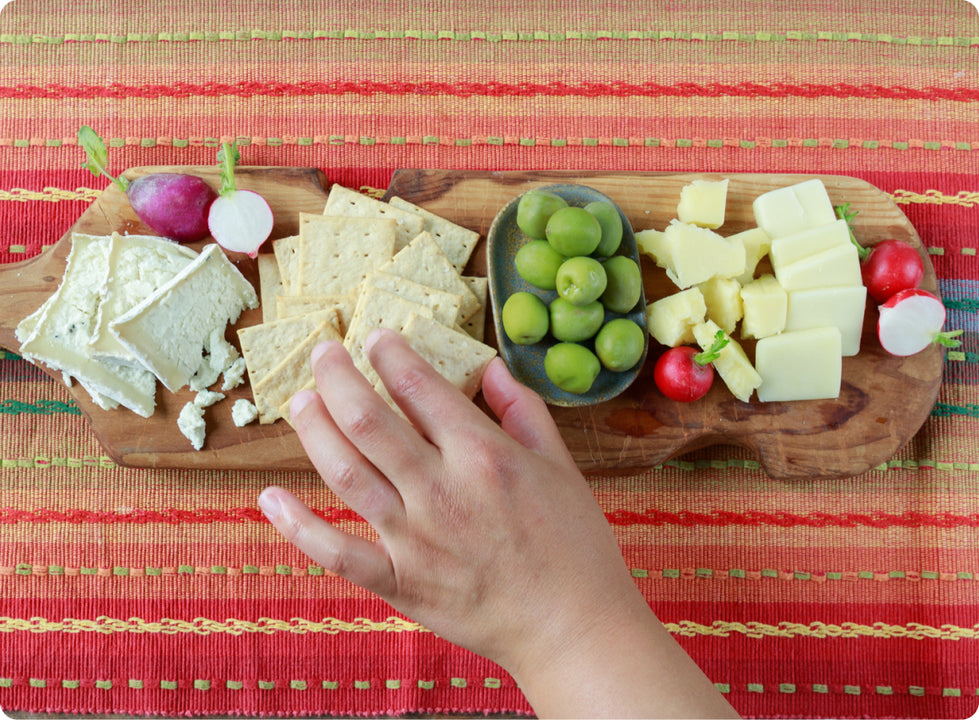 A small kid reaching for a table snack of crackers