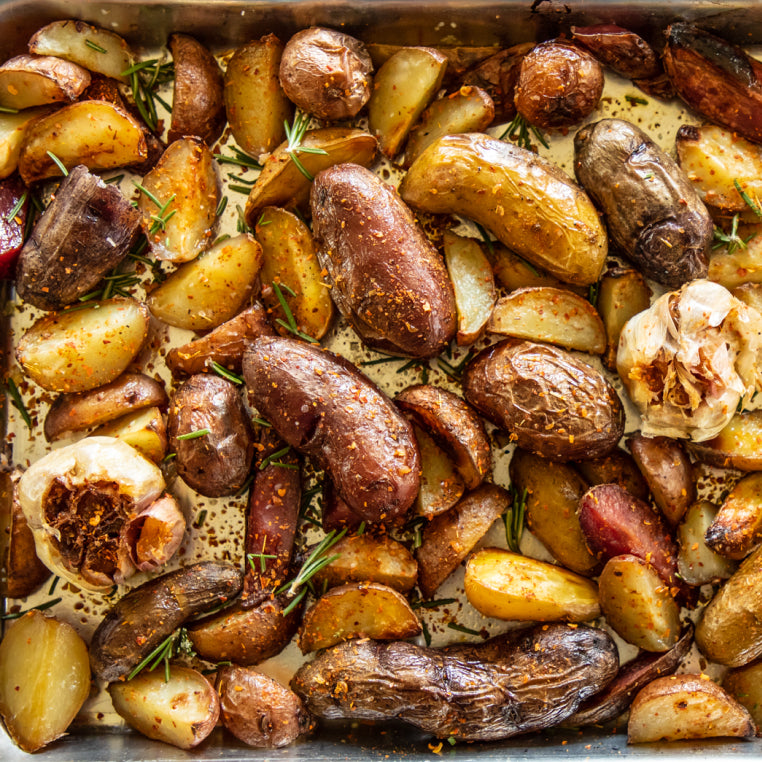 A metal cooking pan filled with roasted potatoes on a dark surface beside a small metal bowl of Patagonia Provisions Aji Molido chile