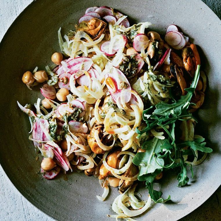 A grey ceramic dish holds salad made with greens, radishes, chickpeas, and Patagonia Provisions mussels