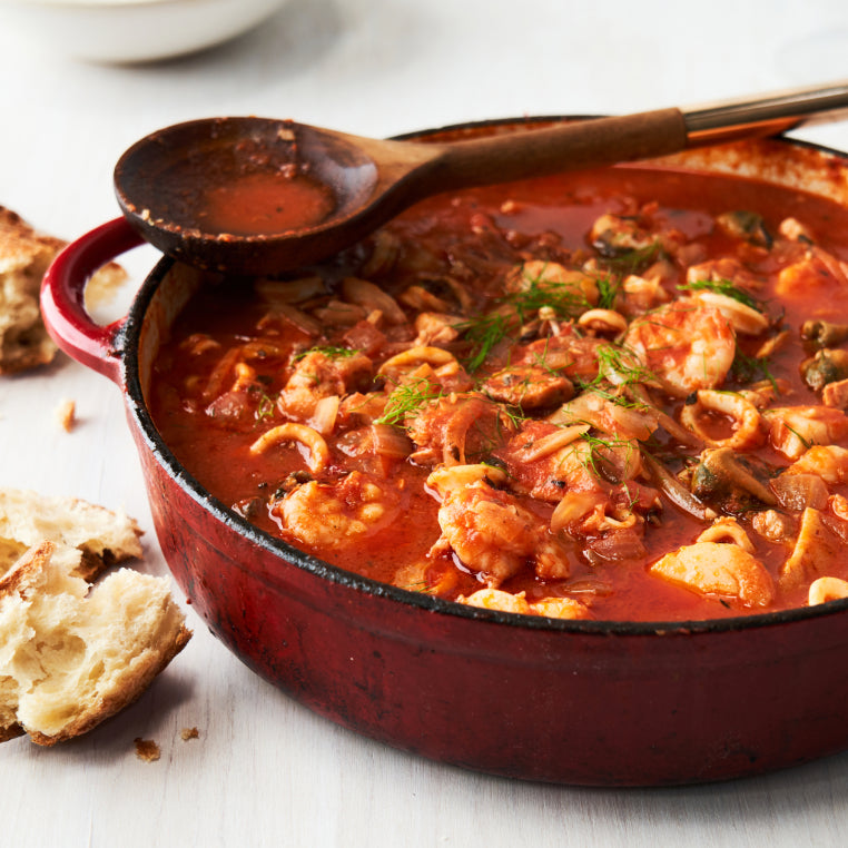 A deep red enamel pot is filled with tomato based seafood soup