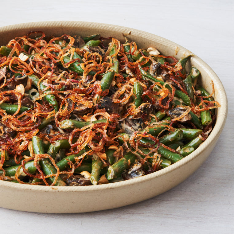 A ceramic casserole dish serves up a creamy green bean casserole topped with crispy shallots
