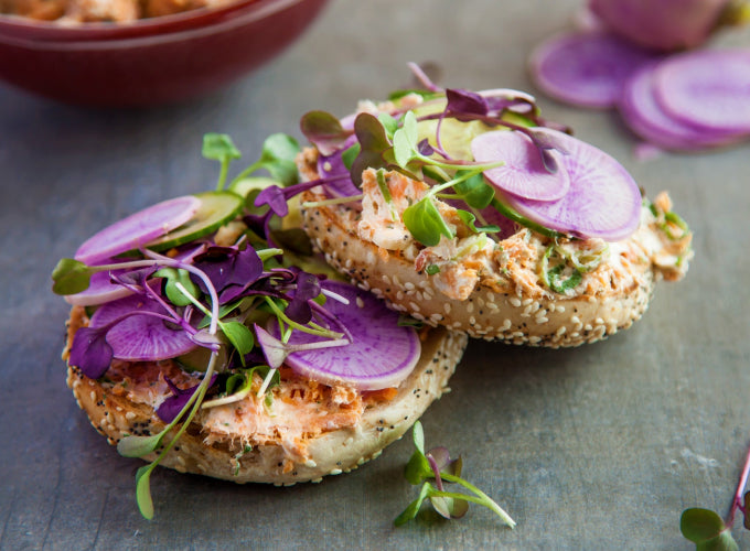 A seeded bagel is topped with Patagonia Provisions Smoked Salmon, purple radishes, and micro greens