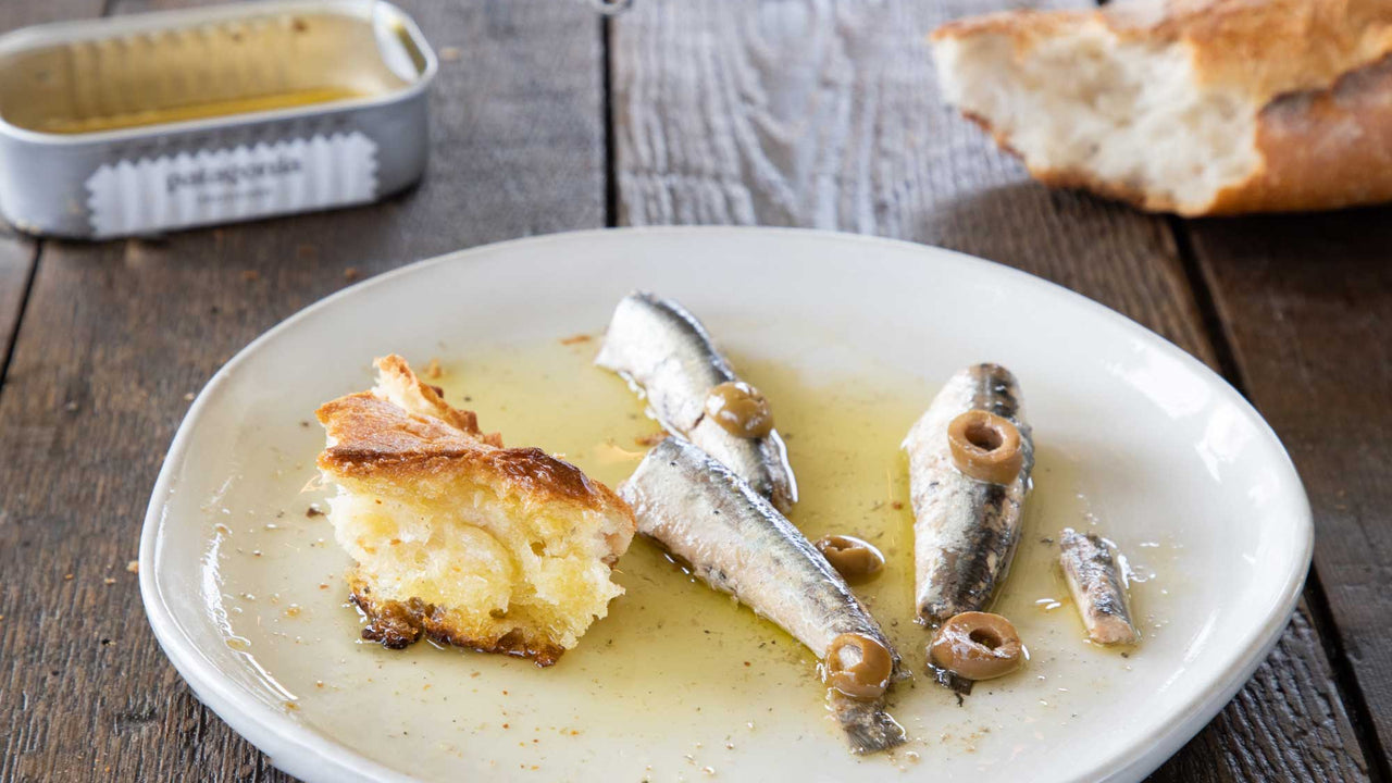 Patagonia Provisions Anchovies with olives, olive oil, and bread on a white ceramic plate