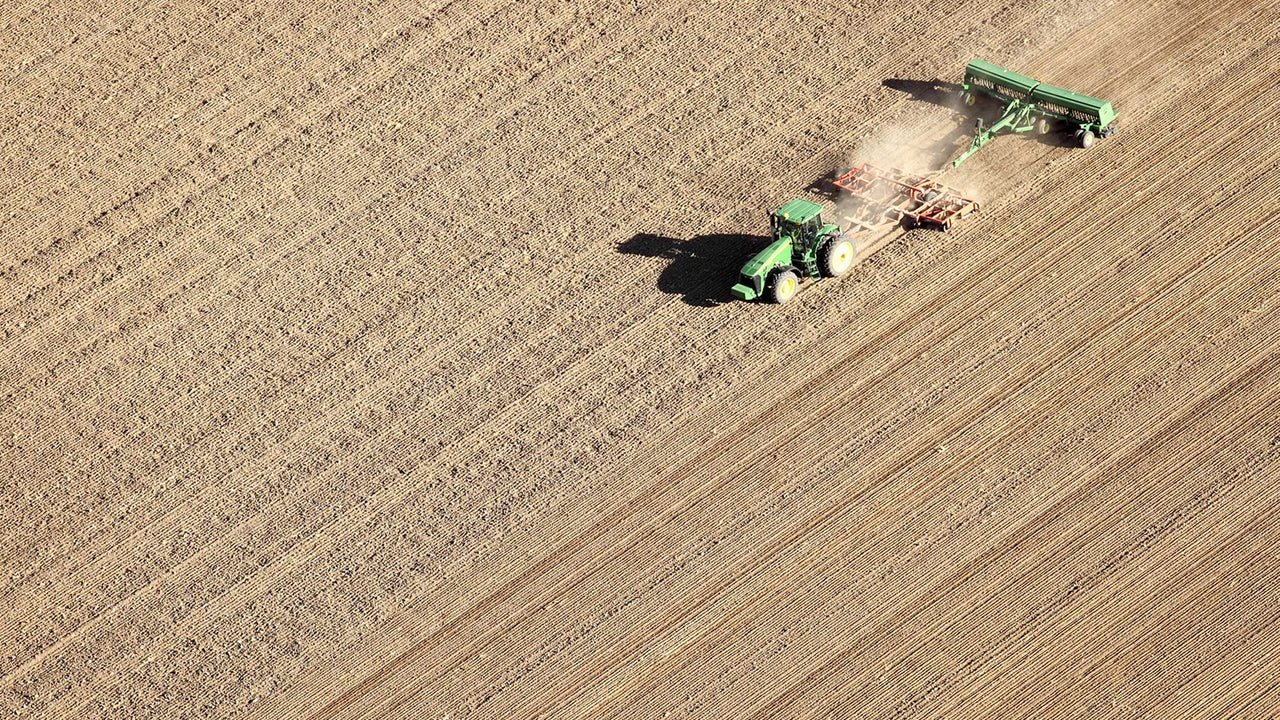 A green tractor tills a brown, dry field